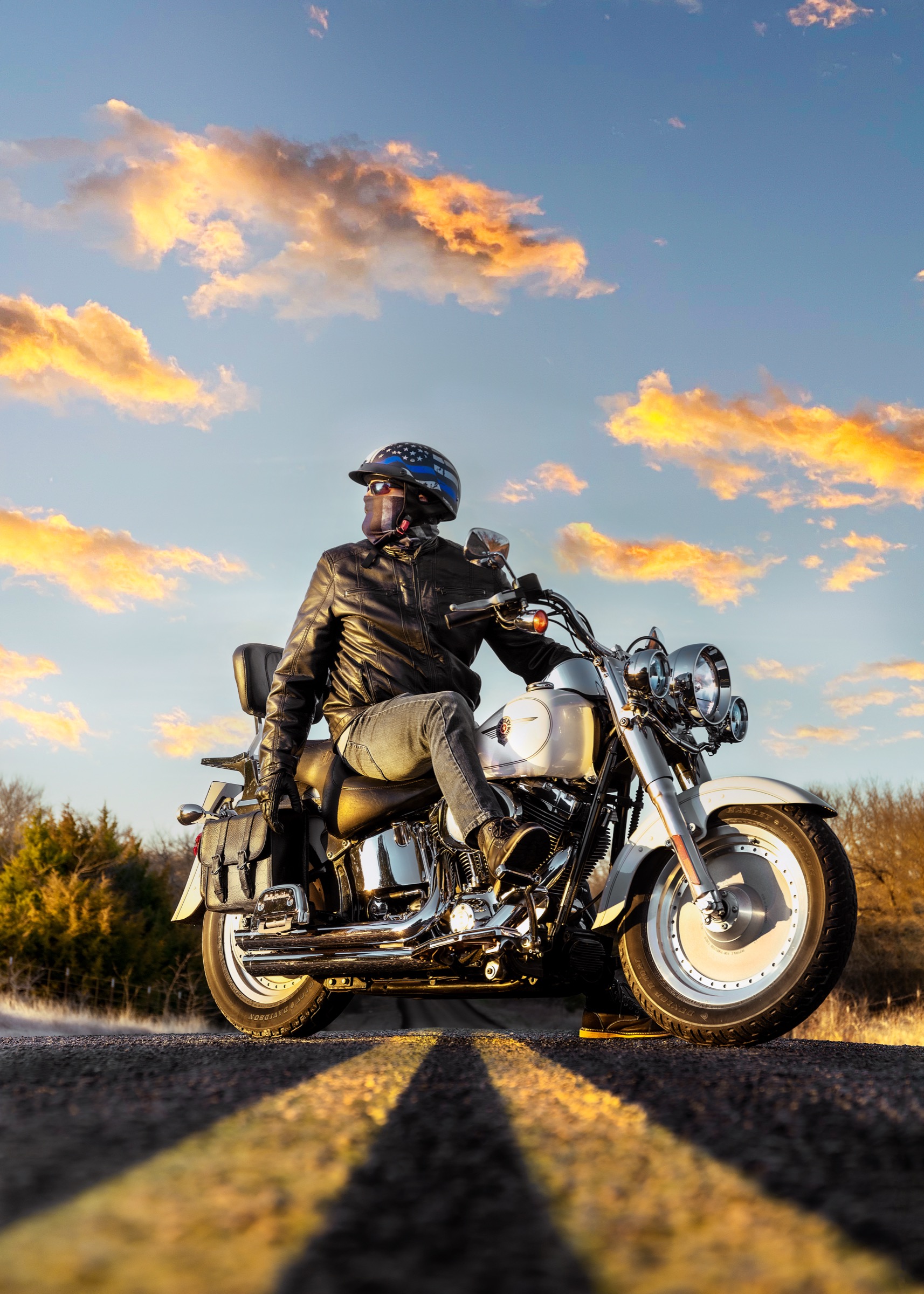 Low-angle portrait of a rider on a motorcycle beneath a blue sky with orange clouds.
