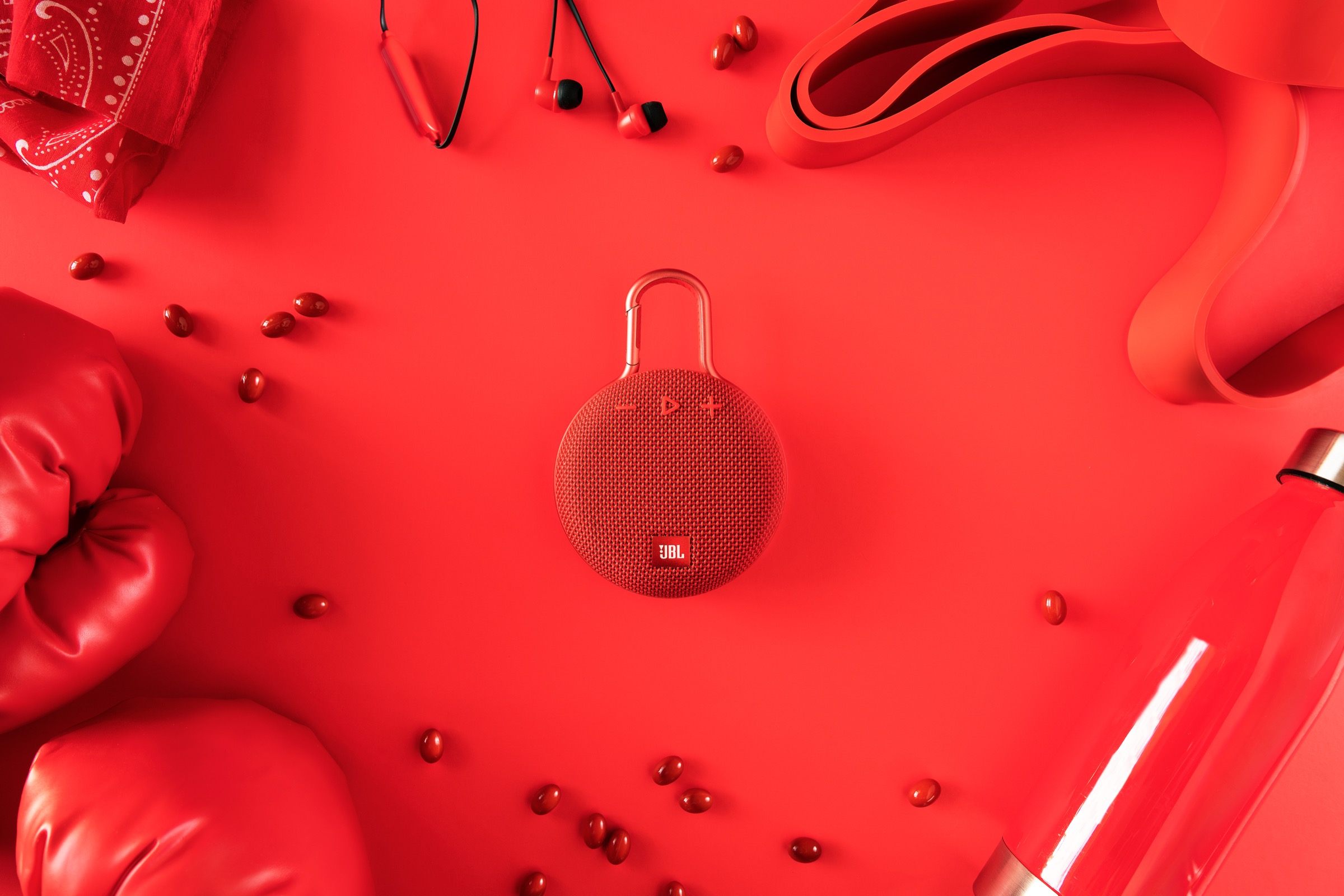 Red portable JBL speaker centered among red props and scattered beads on a red background.